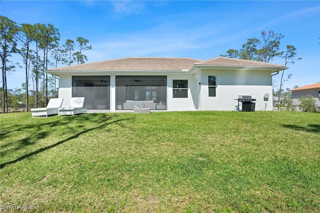 back of property featuring a sunroom, a tile roof, a lawn, and stucco siding