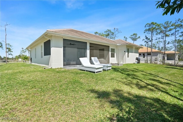 rear view of house with a lawn, a sunroom, and stucco siding