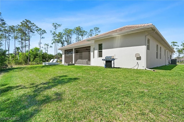 rear view of house with a sunroom, central AC unit, stucco siding, and a yard