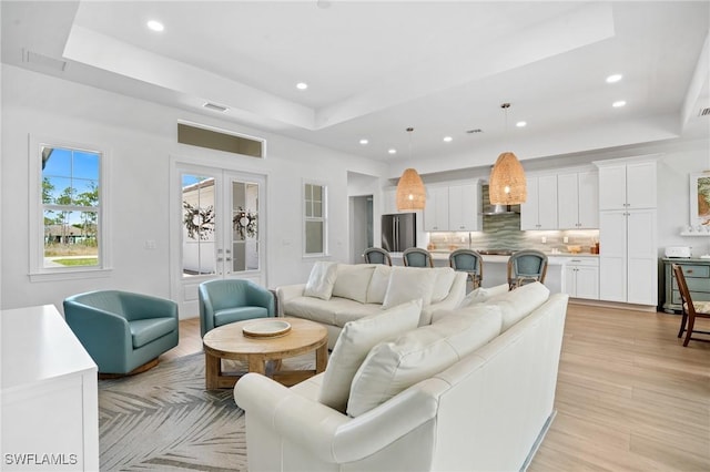 living area featuring light wood-style floors, visible vents, a raised ceiling, and french doors