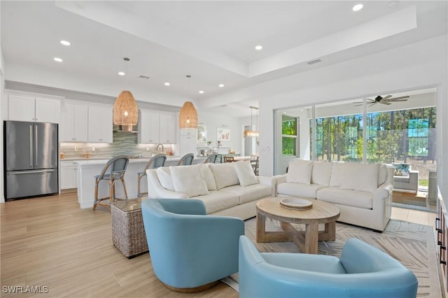 living area featuring light wood-style flooring, visible vents, a tray ceiling, and recessed lighting