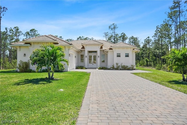 view of front facade featuring an attached garage, a tiled roof, decorative driveway, stucco siding, and a front lawn