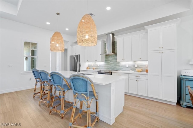 kitchen with stainless steel appliances, a sink, light countertops, wall chimney exhaust hood, and a center island with sink