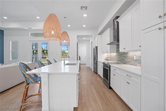 kitchen with stainless steel appliances, visible vents, decorative backsplash, a sink, and wall chimney range hood