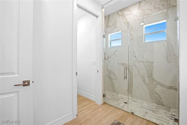 full bath featuring a marble finish shower, baseboards, and wood finished floors