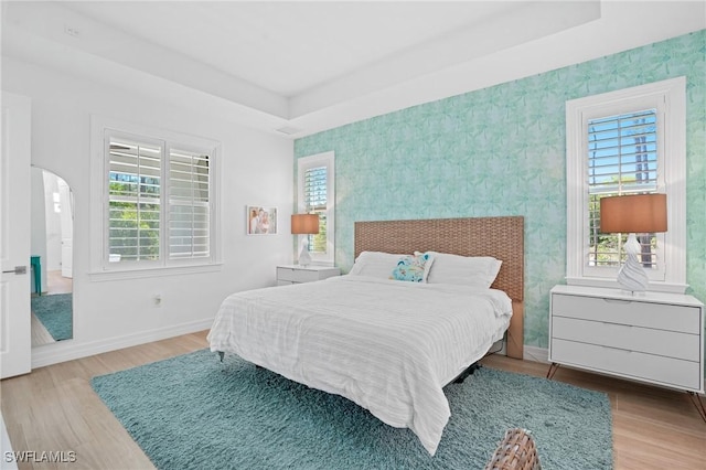 bedroom with arched walkways, baseboards, a tray ceiling, and multiple windows