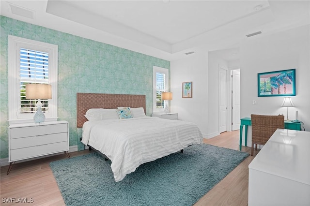 bedroom with a tray ceiling, wood finished floors, visible vents, and baseboards