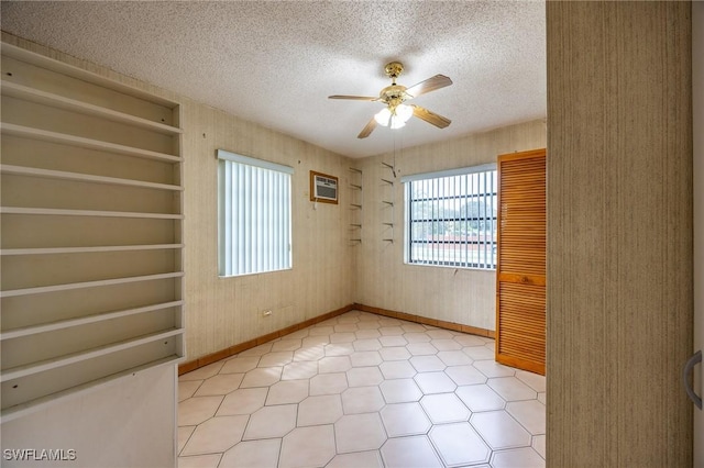 empty room featuring a ceiling fan, a textured ceiling, baseboards, and a wall mounted AC