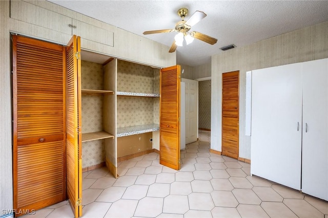 unfurnished bedroom with a textured ceiling, ceiling fan, visible vents, baseboards, and wallpapered walls