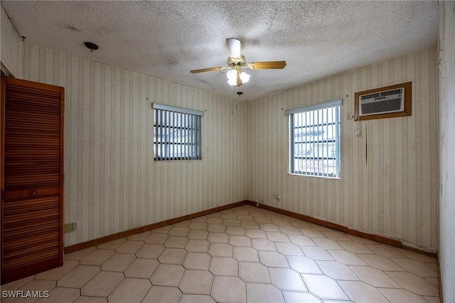 spare room featuring a wall unit AC, wallpapered walls, baseboards, and a textured ceiling