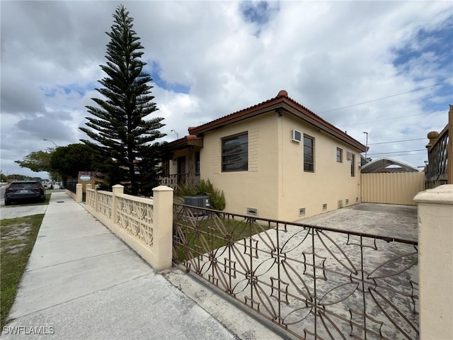 view of side of home featuring a fenced front yard, a tile roof, crawl space, central AC, and stucco siding