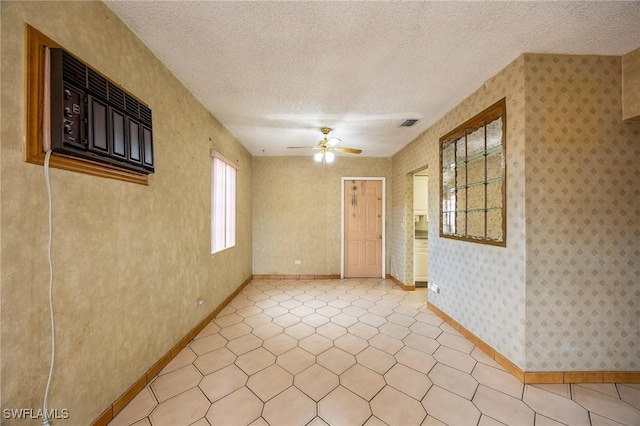 unfurnished room with wallpapered walls, baseboards, visible vents, ceiling fan, and a textured ceiling