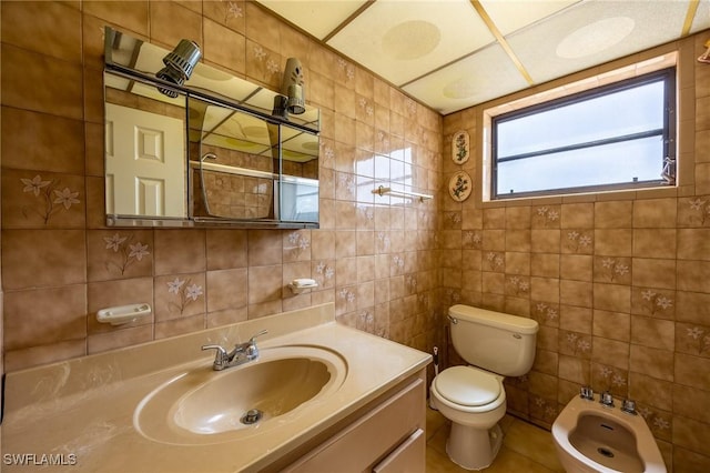 bathroom with toilet, vanity, tile walls, tasteful backsplash, and a bidet