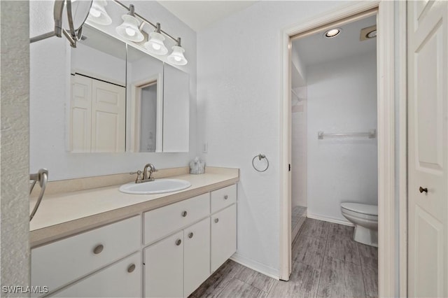 full bath featuring a shower stall, baseboards, wood finish floors, toilet, and vanity