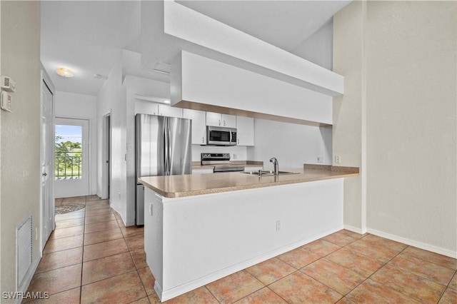 kitchen featuring light tile patterned floors, appliances with stainless steel finishes, a peninsula, white cabinets, and a sink