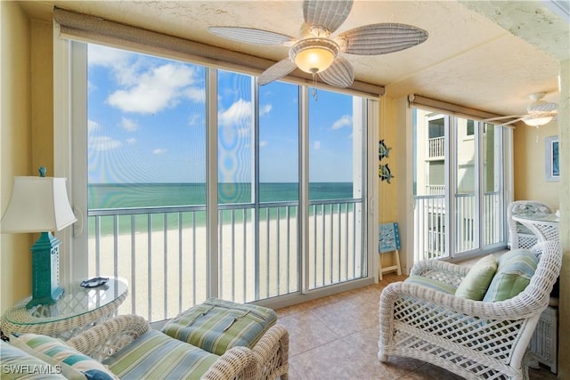 sunroom featuring a view of the beach, ceiling fan, and a water view