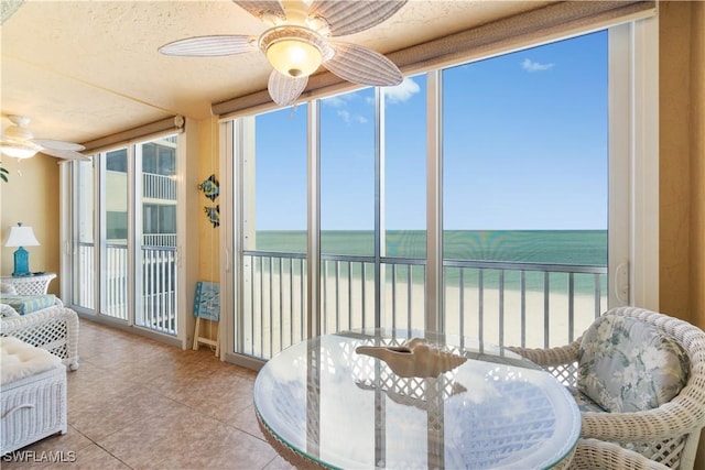 sunroom featuring a beach view, a ceiling fan, and a water view