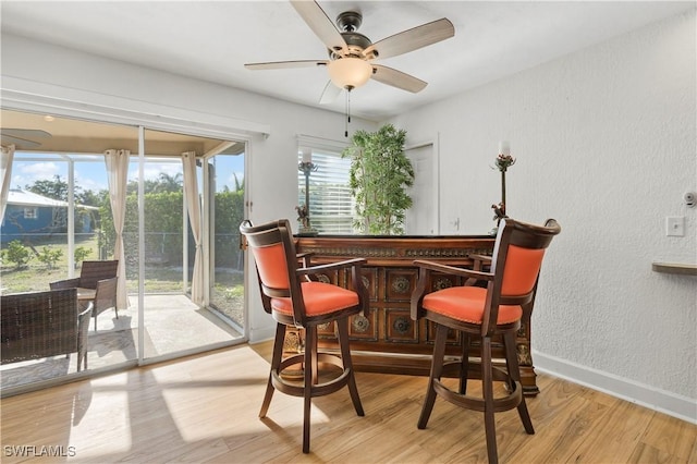 dining space featuring a dry bar, a textured wall, a ceiling fan, wood finished floors, and baseboards