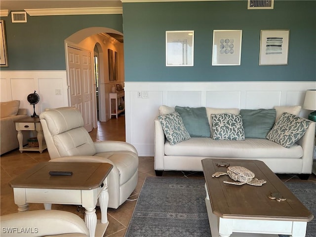 living area with arched walkways, a wainscoted wall, visible vents, tile patterned floors, and crown molding