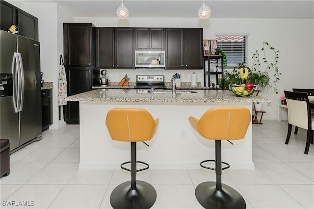 kitchen featuring a kitchen bar, a sink, stainless steel appliances, light tile patterned floors, and light stone countertops