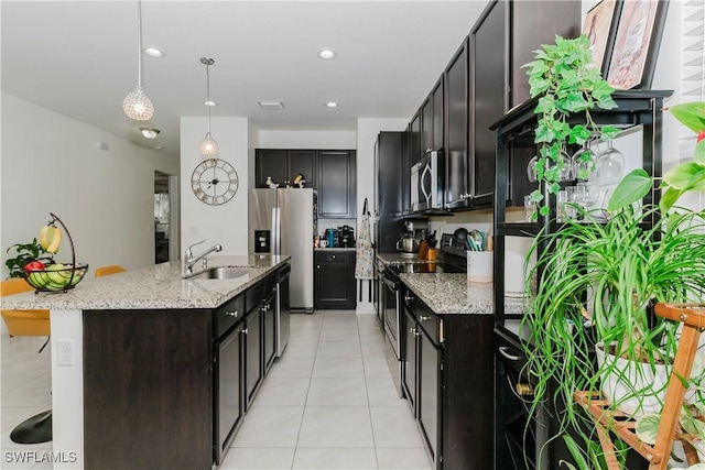 kitchen featuring a center island with sink, light tile patterned flooring, a sink, stainless steel appliances, and decorative light fixtures