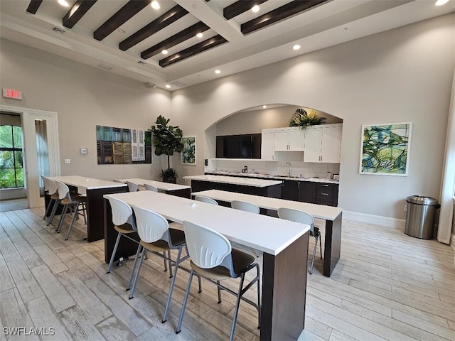 kitchen with a kitchen island, beamed ceiling, light countertops, light wood-style flooring, and a towering ceiling