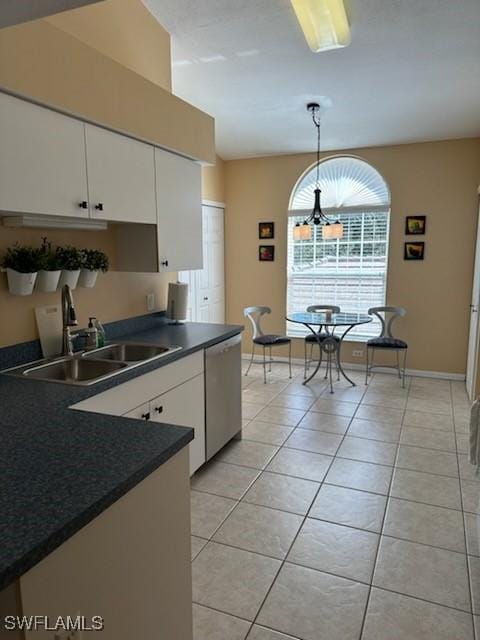 kitchen with light tile patterned floors, dark countertops, white cabinets, a sink, and dishwasher