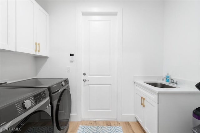 washroom featuring cabinet space, light wood-style flooring, a sink, and washing machine and clothes dryer