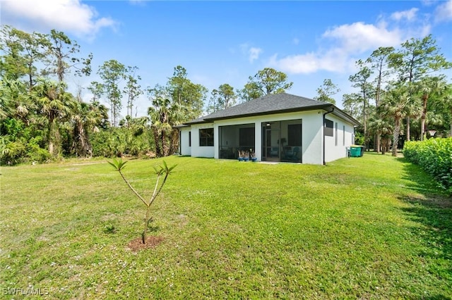 rear view of property with a yard, a sunroom, and stucco siding