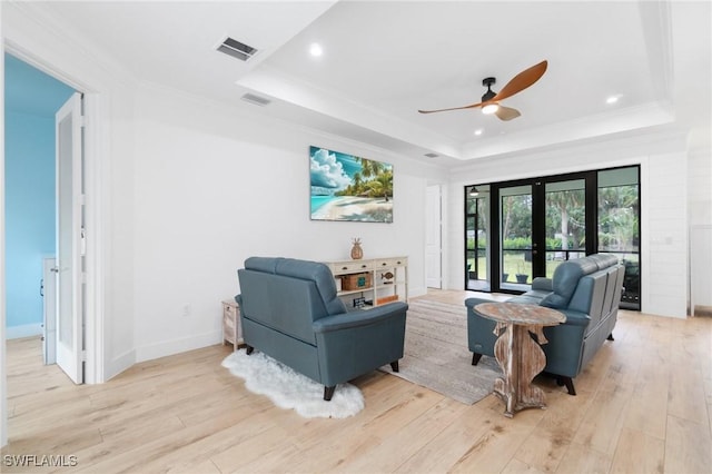 living room featuring a raised ceiling, visible vents, light wood finished floors, and french doors