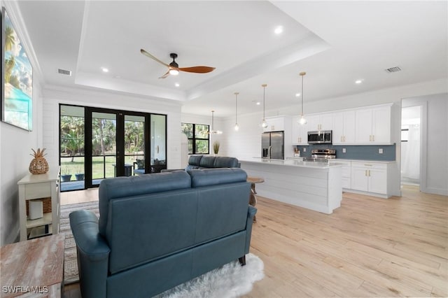 living room featuring a tray ceiling, visible vents, crown molding, and light wood finished floors