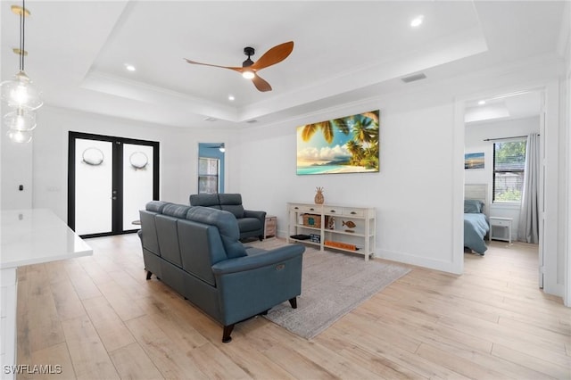 living area with light wood-style flooring, a raised ceiling, and french doors