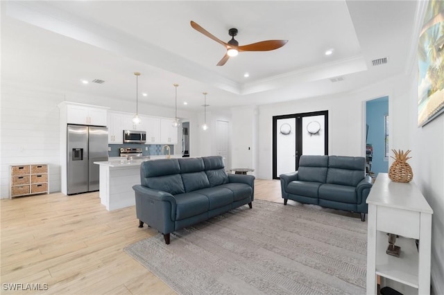 living room featuring ornamental molding, a tray ceiling, visible vents, and light wood-style flooring