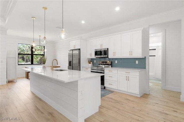 kitchen featuring appliances with stainless steel finishes, a kitchen island with sink, a sink, and ornamental molding