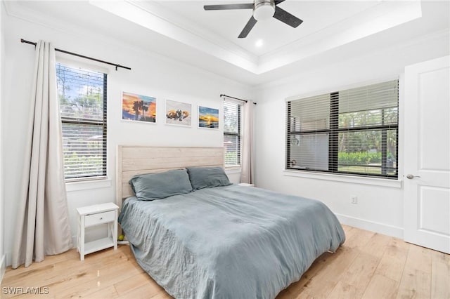 bedroom with ornamental molding, a raised ceiling, baseboards, and light wood finished floors