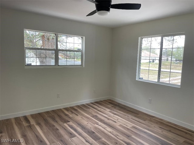 empty room featuring plenty of natural light, wood finished floors, a ceiling fan, and baseboards