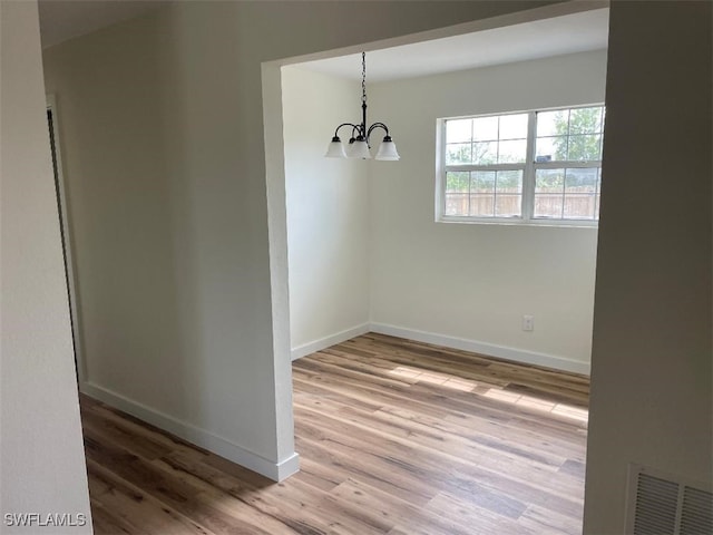 unfurnished dining area featuring an inviting chandelier, baseboards, visible vents, and wood finished floors