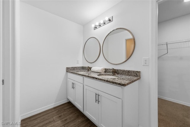 full bath featuring a sink, baseboards, wood finished floors, and double vanity