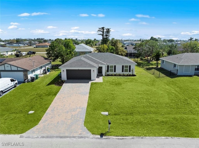 ranch-style house featuring fence, an attached garage, a front lawn, decorative driveway, and a residential view