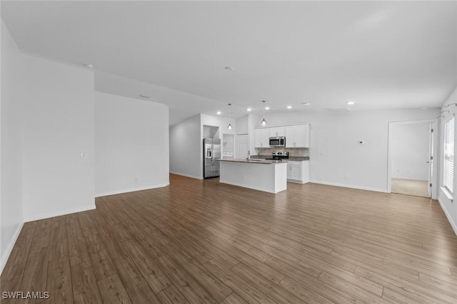 unfurnished living room with recessed lighting, baseboards, wood finished floors, and a sink