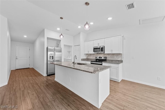 kitchen with visible vents, a sink, appliances with stainless steel finishes, decorative backsplash, and light stone countertops