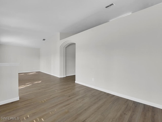 unfurnished room featuring baseboards, visible vents, arched walkways, and wood finished floors