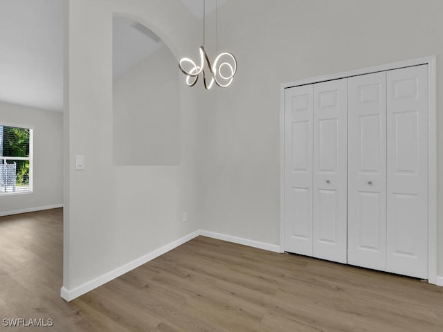 unfurnished dining area with a chandelier, baseboards, and wood finished floors