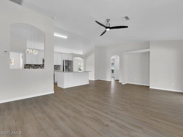 unfurnished living room with arched walkways, ceiling fan, wood finished floors, visible vents, and baseboards