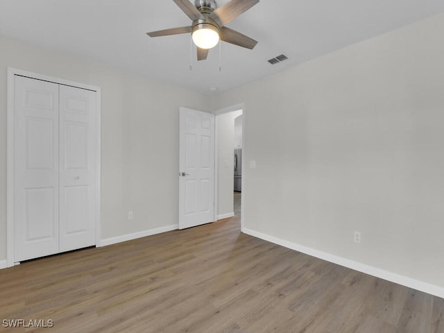 unfurnished bedroom featuring wood finished floors, a ceiling fan, visible vents, baseboards, and a closet