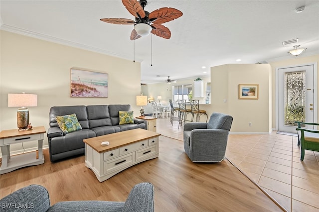 living area featuring visible vents, crown molding, baseboards, ceiling fan, and light wood-style flooring