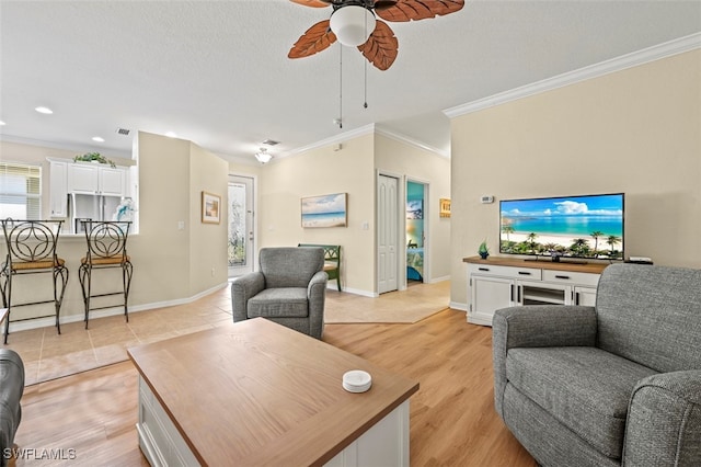 living area featuring ceiling fan, light wood-style flooring, baseboards, and ornamental molding