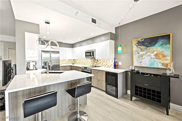 kitchen featuring a sink, light stone counters, tasteful backsplash, stainless steel appliances, and wine cooler