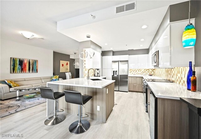 27091 Lake Harbor Ct Unit 102, Bonita Springs, FL 34134 - kitchen featuring stainless steel appliances, modern cabinets, a sink, a kitchen breakfast bar, and light wood-style flooring