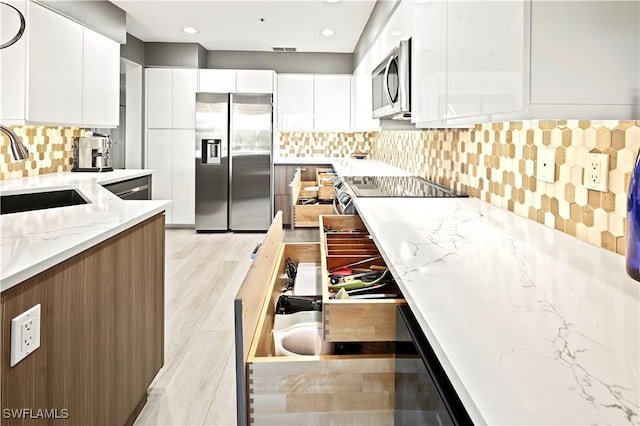 kitchen featuring modern cabinets, a sink, light stone counters, appliances with stainless steel finishes, and white cabinets